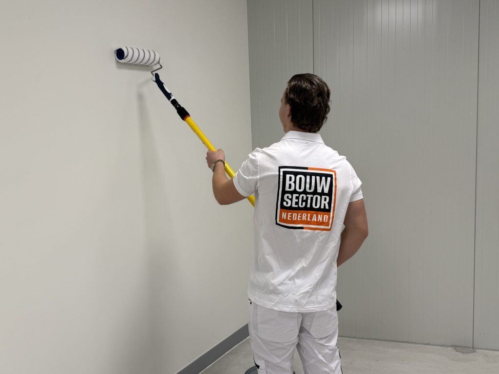 Schilder zet met een roller aan een gele steel een baan muurverf op een witte wand