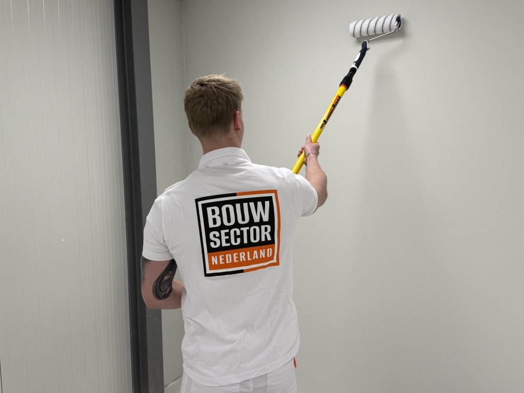 Schilder rolt verf op een lichte wand in een smalle ruimte naast een deurpost