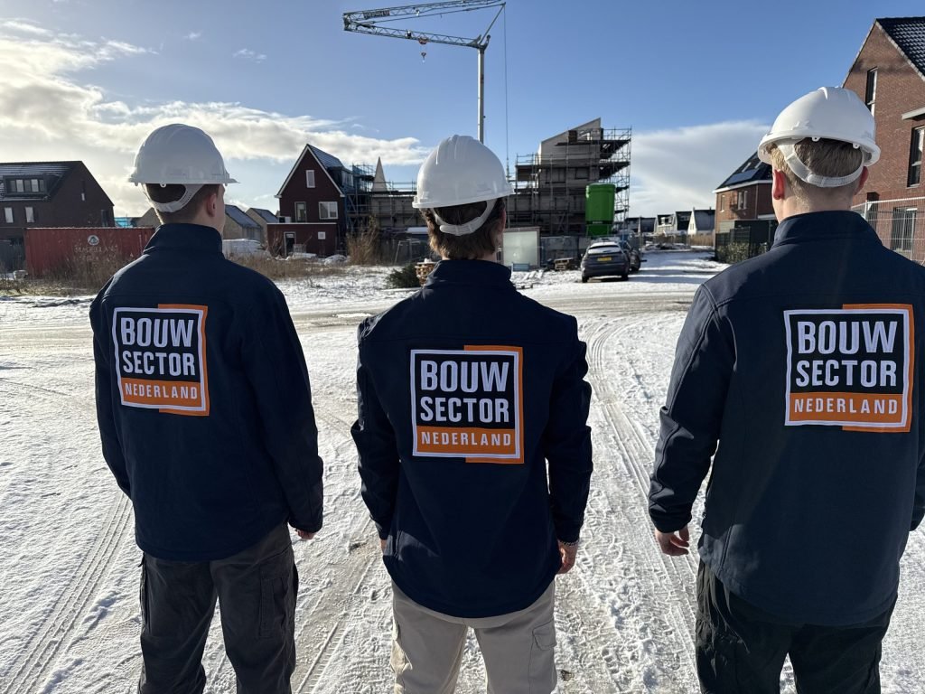 Drie mensen van Bouwsector Nederland op de rug gezien, met witte helm, voor een rij nieuwe woningen in aanbouw