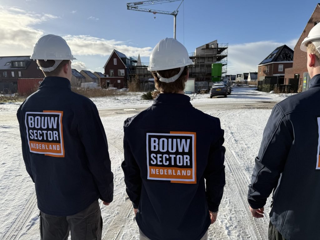 Vakmensen van Bouwsector Nederland met witte helm en donkere jas op een besneeuwde weg tussen bakstenen woningen